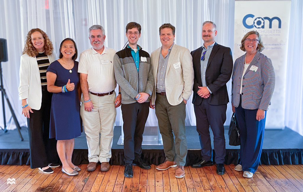 Multiscale Systems accepts M2I2 award in Holyoke on July 11, 2024. Left to right standing in front of a podium with a CAM banner is Christine Nolan (Director, Center for Advanced Manufacturing), Yvonne Hao (Massachusetts Secretary of Economic Development), John McCarthy (Corporate Development Specialist, Quinsigamond Community College), Jesse Silverberg (CEO/Research Director, Multiscale Systems), Zak Dutton (Executive Director, Venture Forum), Patrick Royce (VP Business Lending, Webster Five), Carolyn Kirk (CEO, MassTech Collaborative).