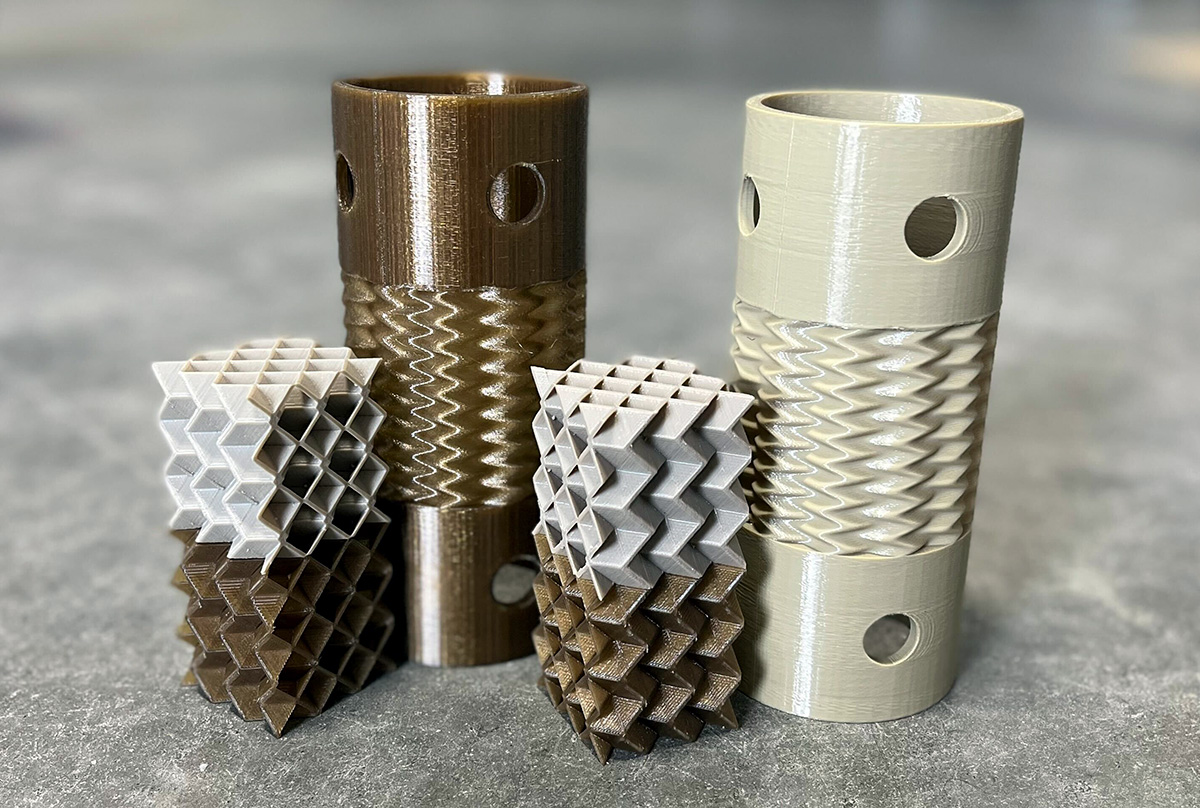 PEEK 3D printed prototypes, two taller cyclindrical parts and four smaller cubes. Half the parts are a lighter color after being heat treated, or annealed.