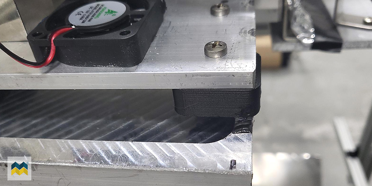 A captured metal 3D printed part made of carbon fiber thermoplastic is screwed into place on a machine using a bolt and the embedded nut.